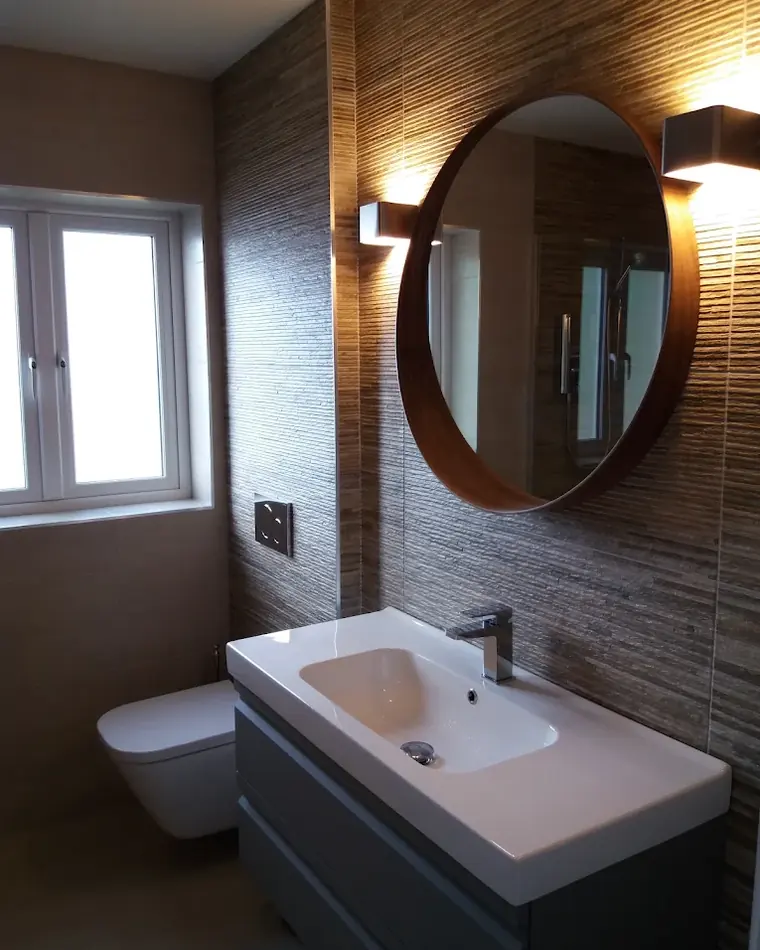 Finished bathroom with a wall-hung toilet, vanity unit and round mirror
